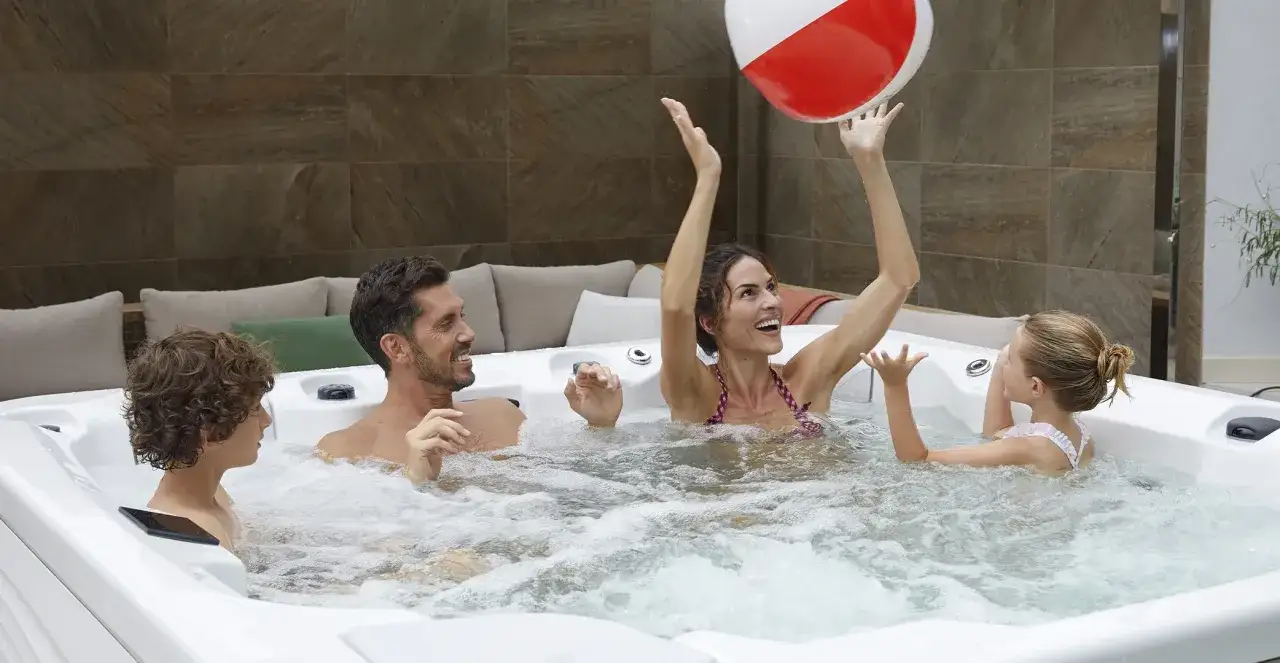 Rodzina bawi się w jacuzzi. Od jakiego wieku dzieci mogą korzystać z jacuzzi? Wszyscy wyglądają na szczęśliwych, grając w piłkę.