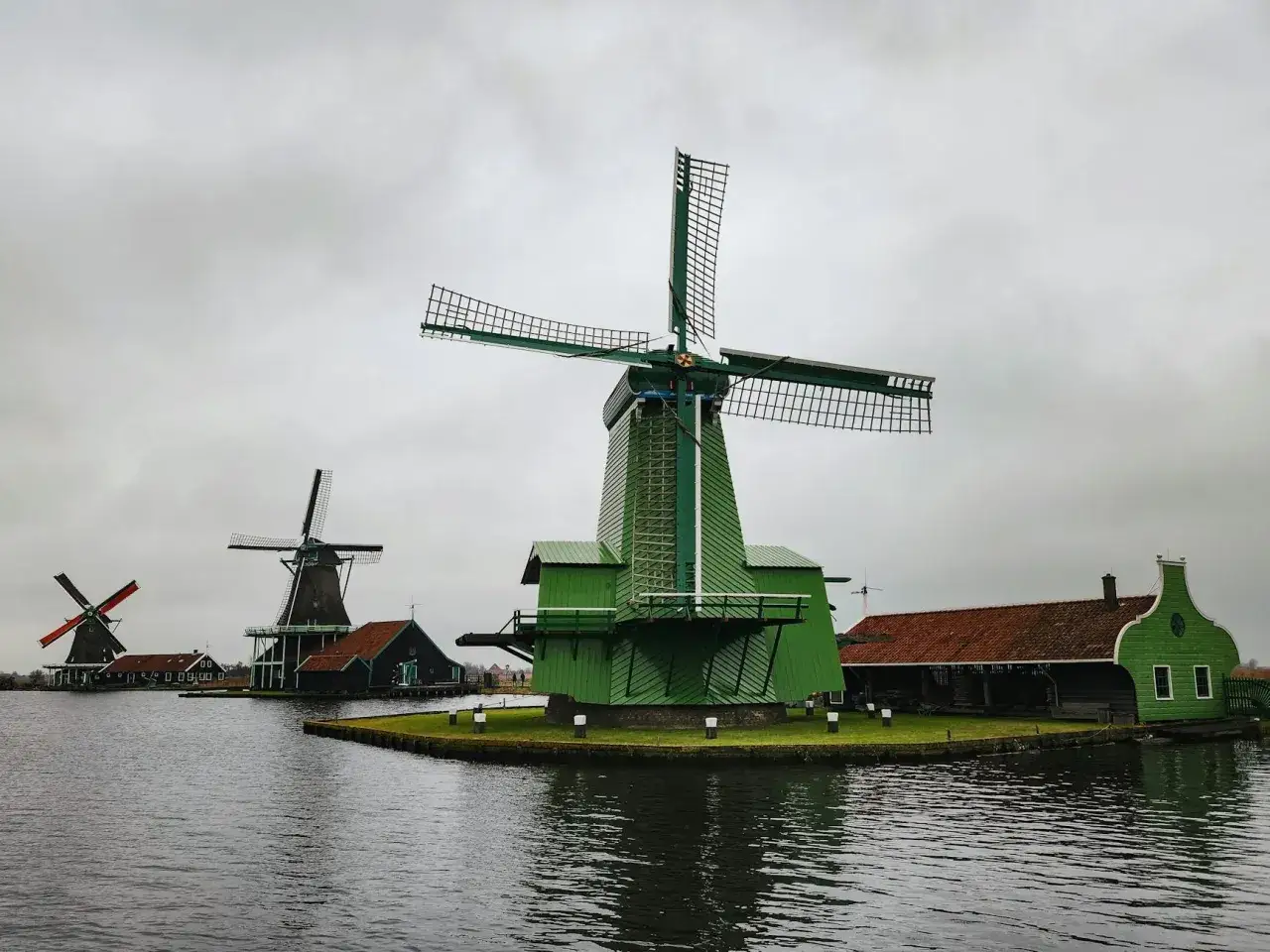 Wiatraki w Zaanse Schans, zielone i brązowe, stoją nad wodą.