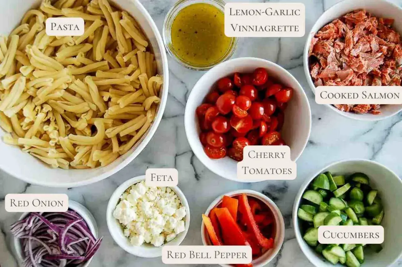 Ingredientes para una ensalada de pasta con salmón: pasta, salmón cocido, tomates cherry, pepino, pimiento rojo, cebolla roja, queso feta y vinagreta de limón y ajo.