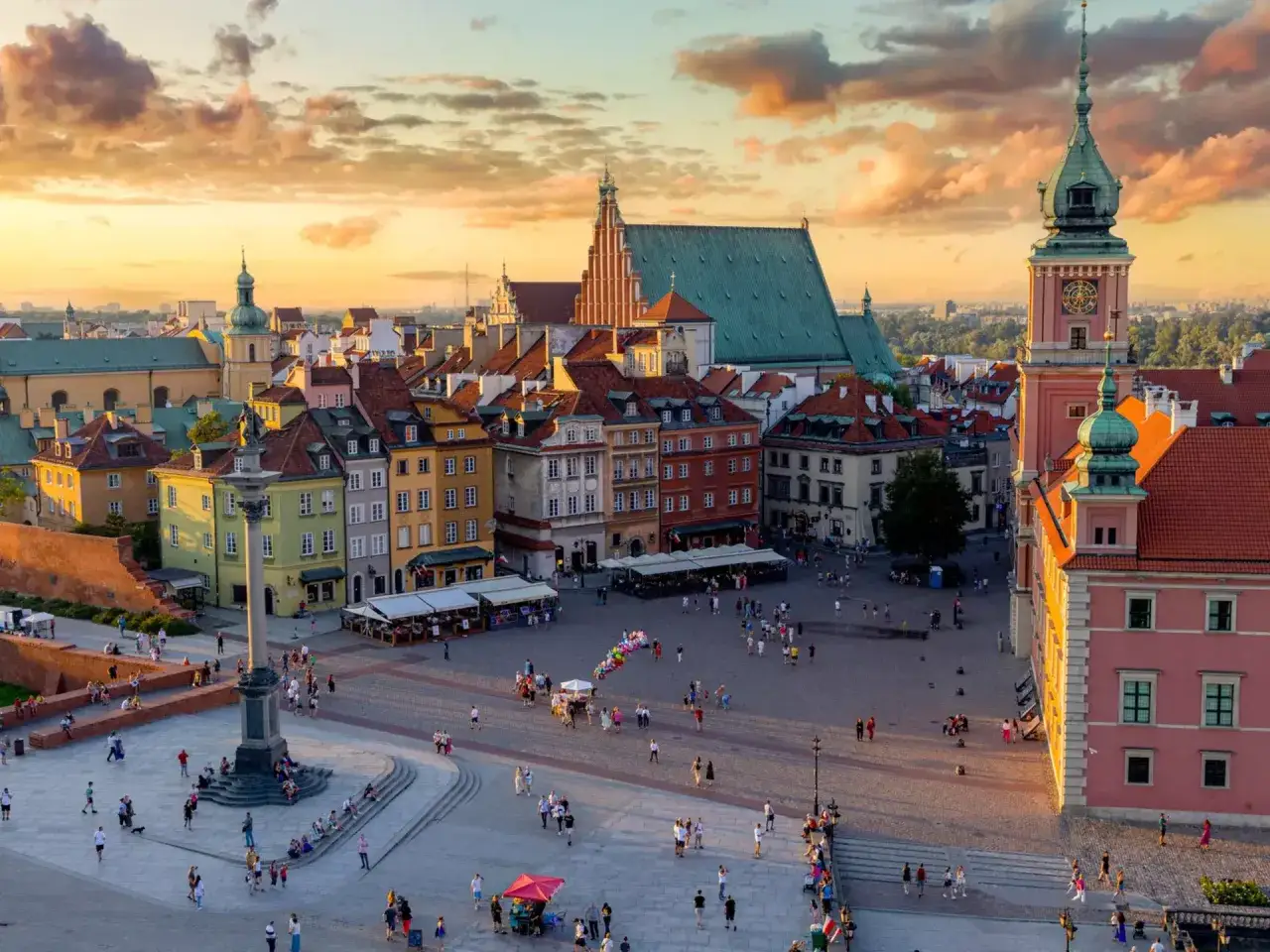Warschau im Abendlicht: bunte Häuser, ein Platz mit Menschen und ein Turm. Perfekt für die beste Reisezeit Polen.