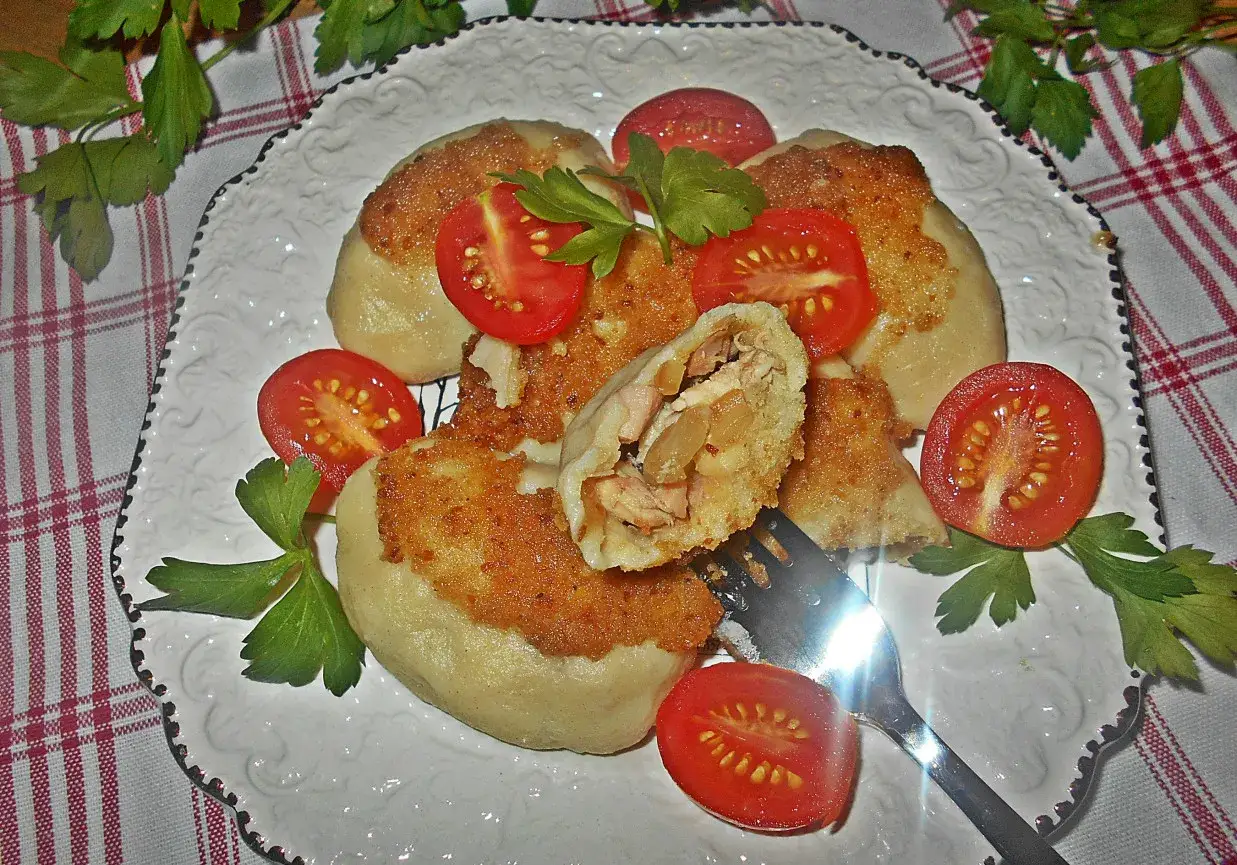 Pyszne gnocchi z kurczakiem, podsmażone na złoto, podane z pomidorkami i natką pietruszki. Jedno gnocchi jest przekrojone, ukazując soczyste nadzienie.