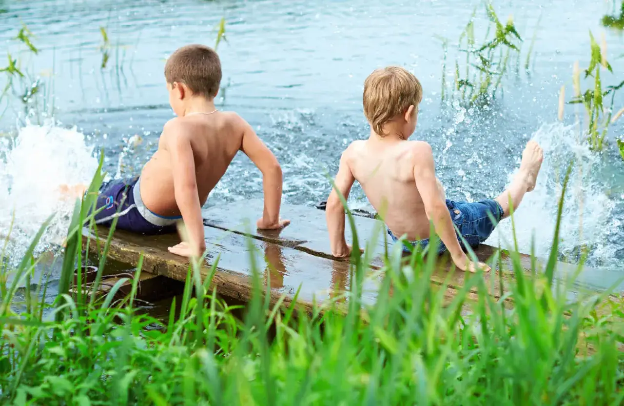 Two boys enjoy the water, splashing and kicking their legs. This scene captures the essence of parallel play, where children play alongside each other without direct interaction.