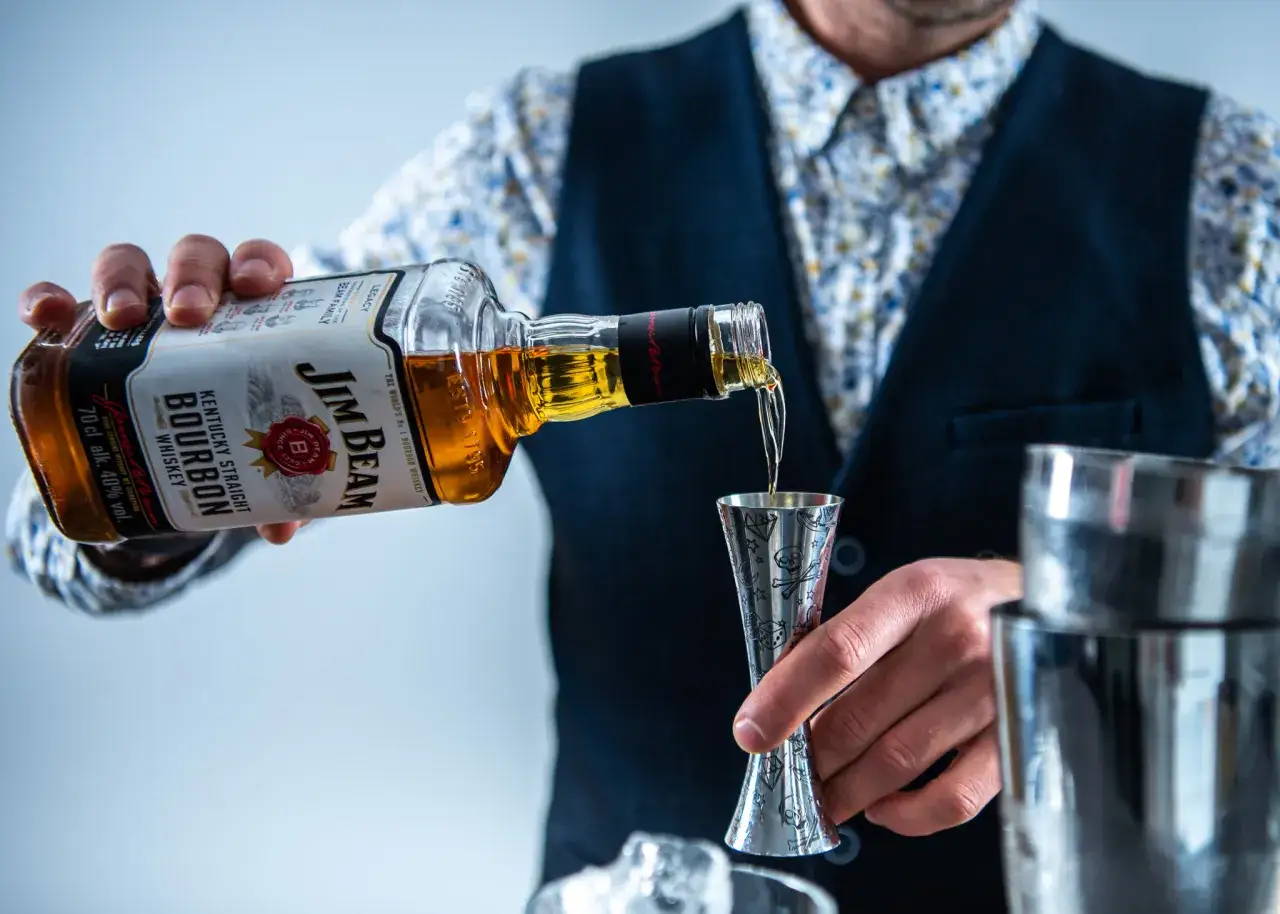 Barman nalewa bourbon do jiggera, odmierzając idealną ilość soku z cytryny do whiskey sour.
