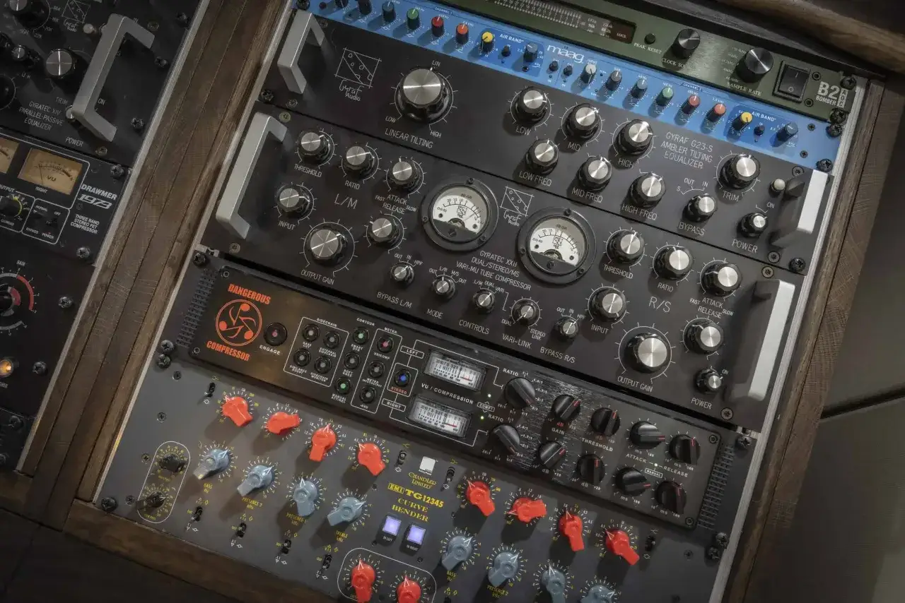 Rack d'équipement audio professionnel pour le mixage et mastering, avec égaliseurs, compresseurs et VU-mètres.