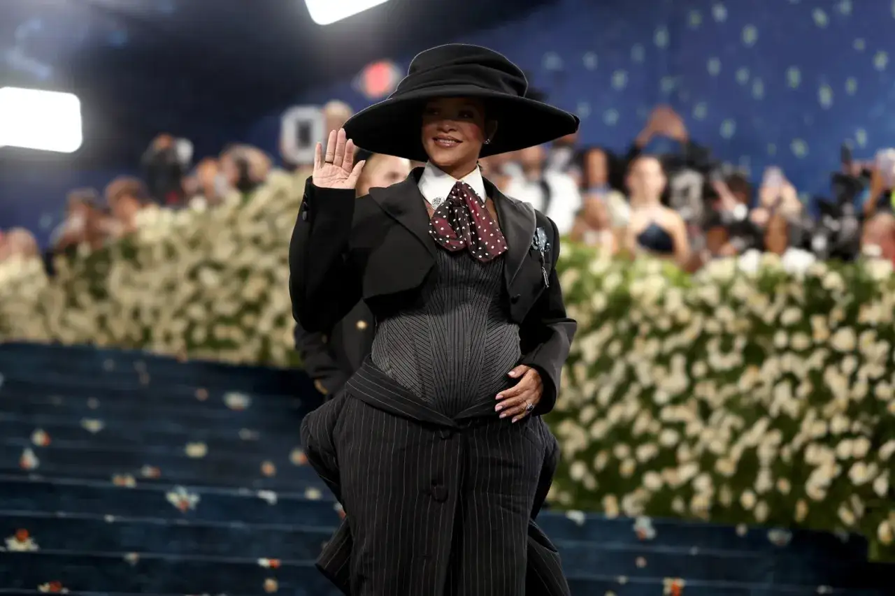 Rihanna w ciąży, w eleganckim czarnym kapeluszu i stylizacji, pozdrawia tłum.