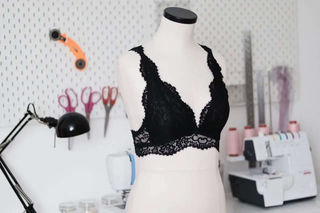 Czarny koronkowy bralet na manekinie, obok maszyna do szycia i akcesoria krawieckie. Idealne miejsce, by dowiedzieć się, jak uszyć bralet.