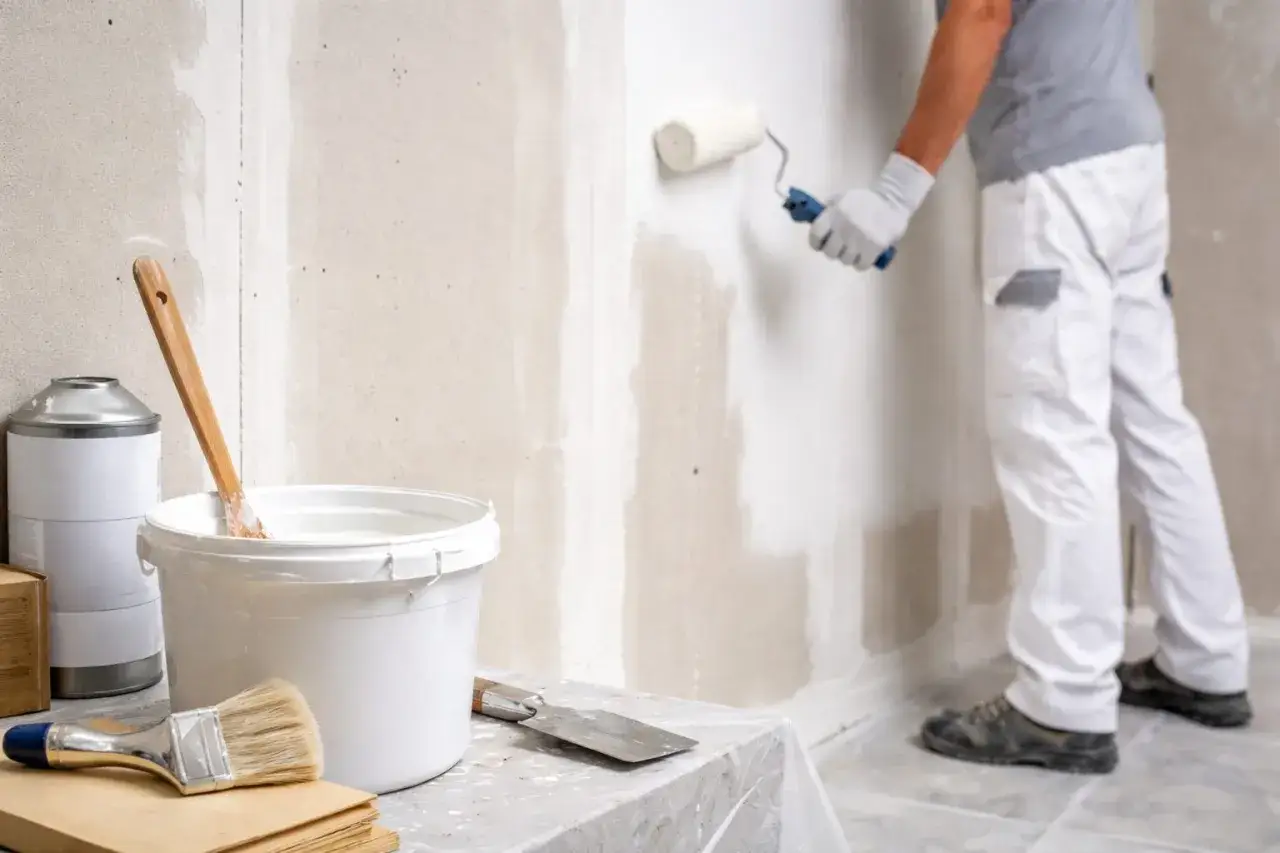 Un peintre applique de la peinture sur un mur en Fermacell avec un rouleau. Mat&eacute;riel de peinture &agrave; proximit&eacute;.