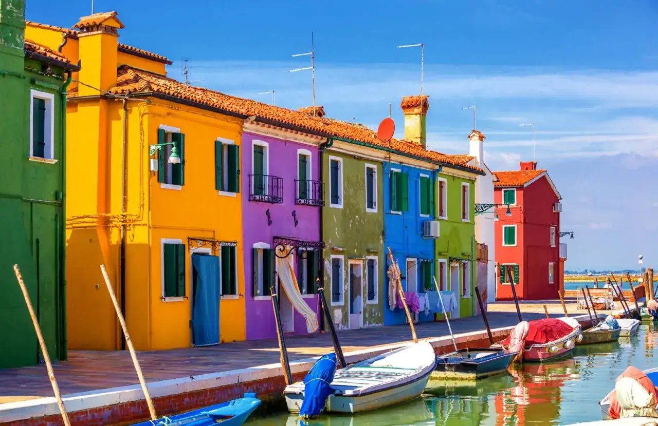 Case colorate a Burano, un'isola di Venezia, con barche ormeggiate e turisti che passeggiano.