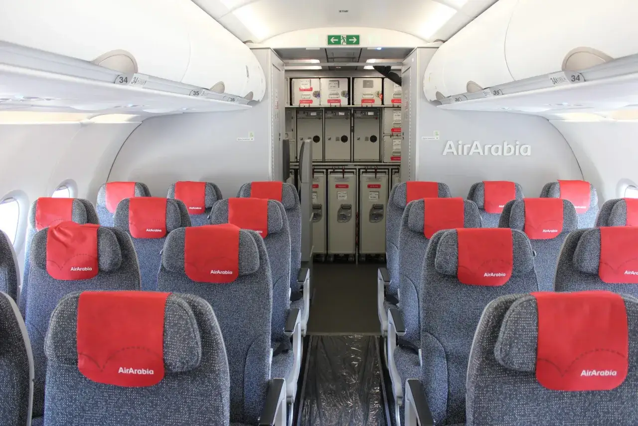 Wnętrze samolotu Air Arabia z rzędami szarych siedzeń i czerwonymi zagłówkami. W tle widać wózki pokładowe. Dobre opinie o Air Arabia potwierdzają komfort podróży.