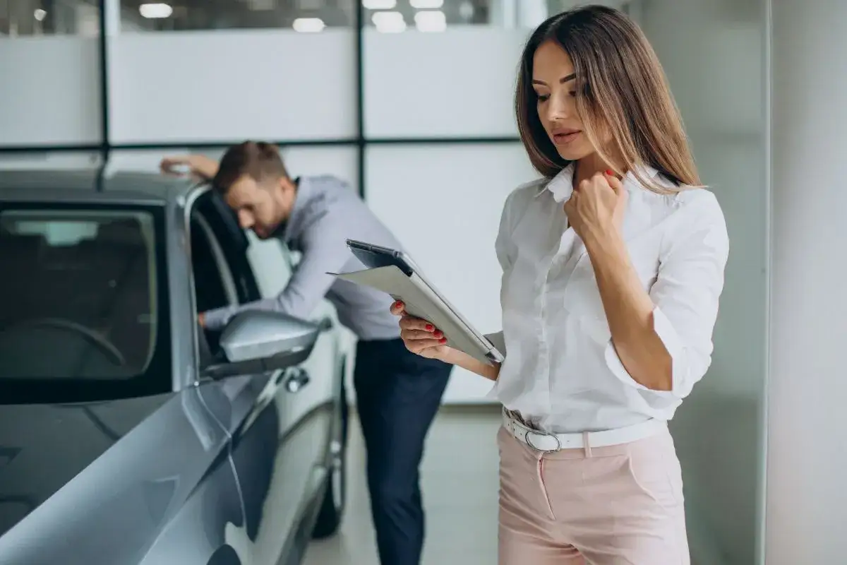 Kobieta z tabletem analizuje ofertę mbank leasing, podczas gdy mężczyzna ogląda nowy samochód.