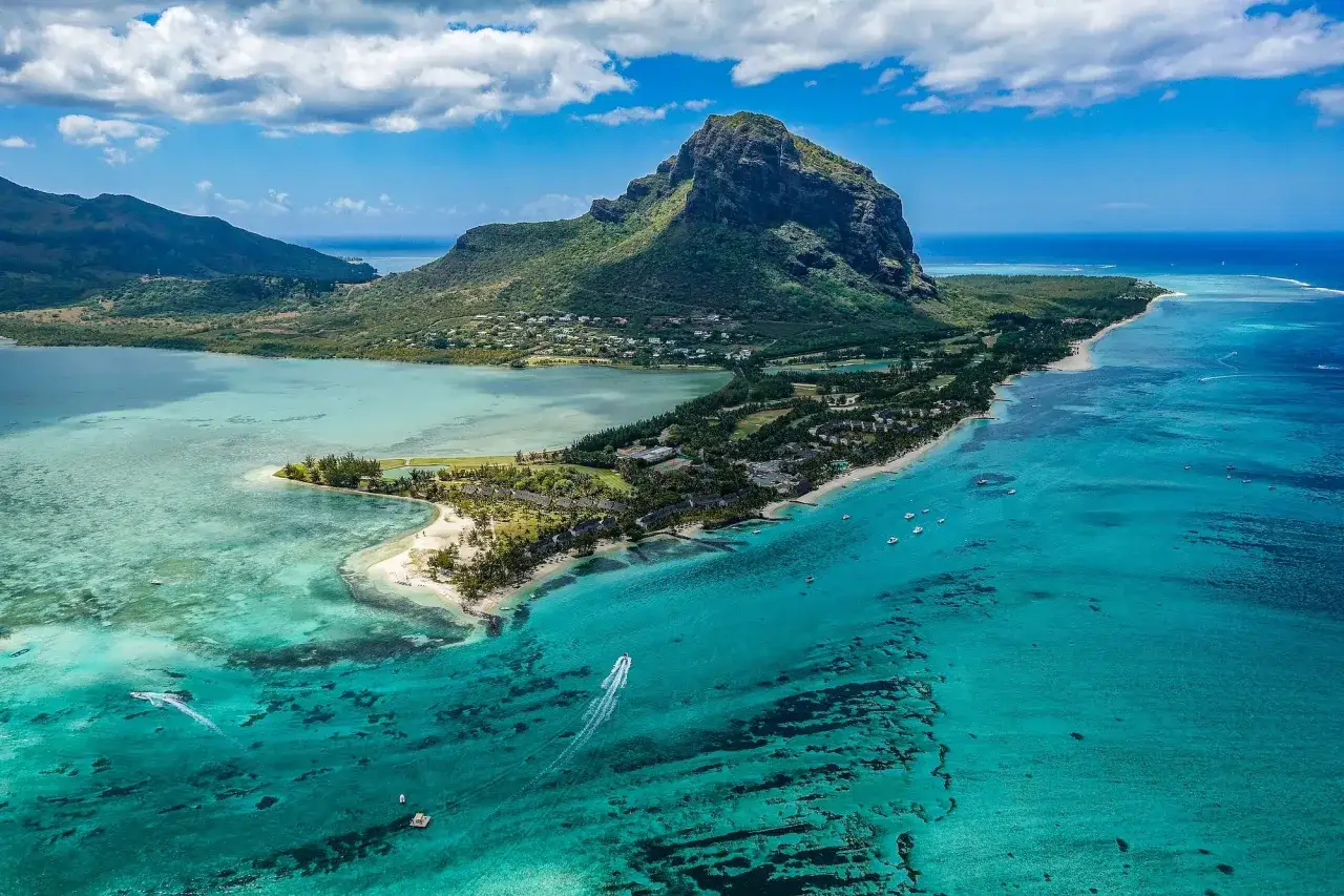Widok z lotu ptaka na g&oacute;rzysty krajobraz i turkusowe wody, gdzie leży Mauritius. Widać plaże, hotele i łodzie.