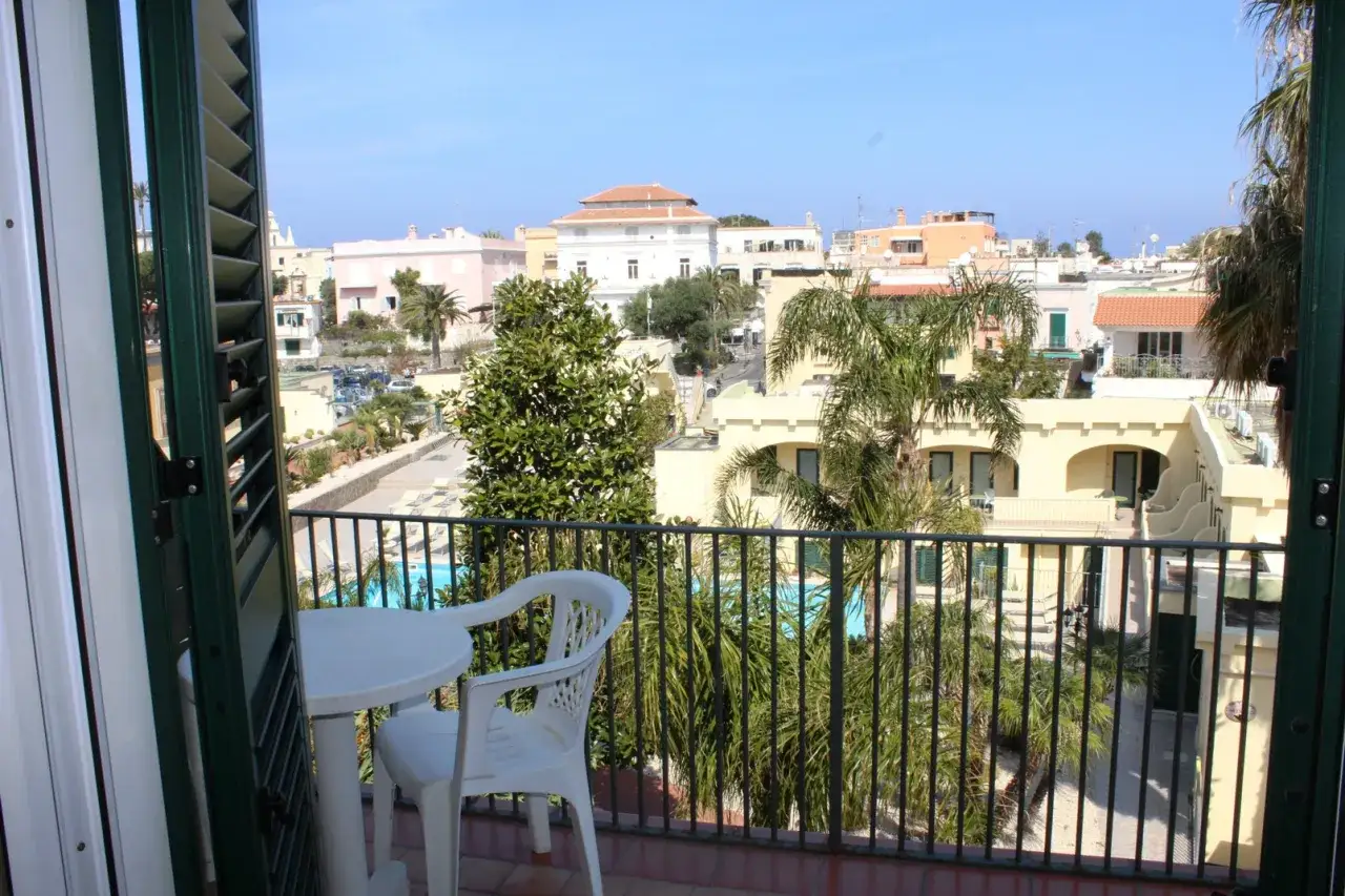 Balcone con tavolo e sedia, vista su piscina e edifici colorati. Le recensioni per hotel terme punta del sole sembrano positive.