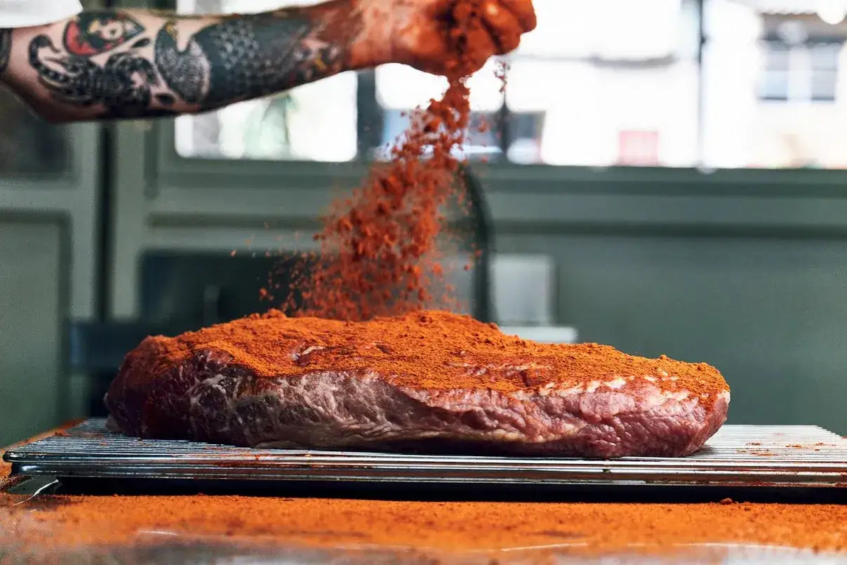 Un trozo de carne cruda, que ser&aacute; pastrami, se cubre con una generosa capa de especias rojas.