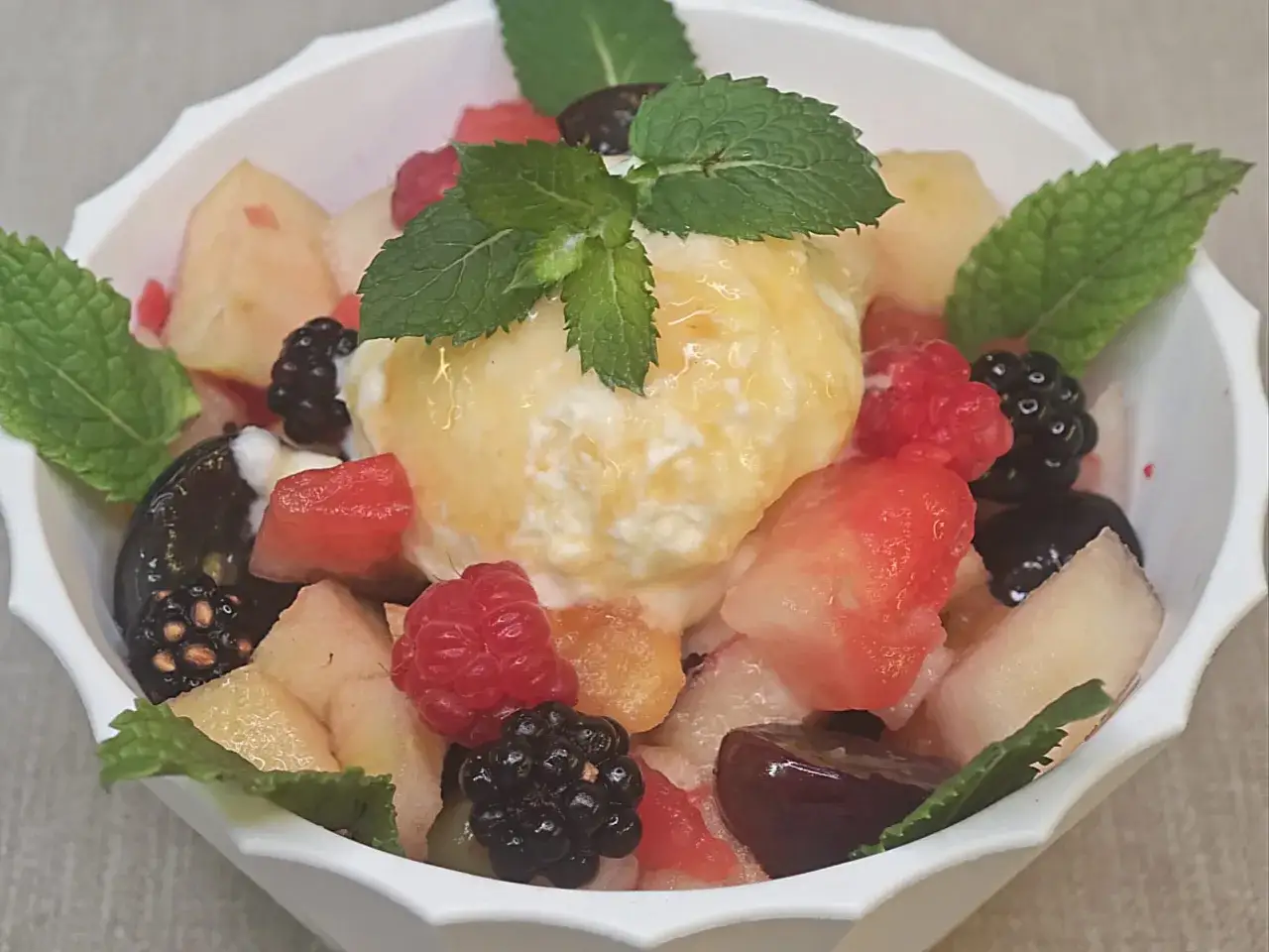 Macedonia di frutta fresca con gelato alla vaniglia, lamponi, more, pesche e menta.