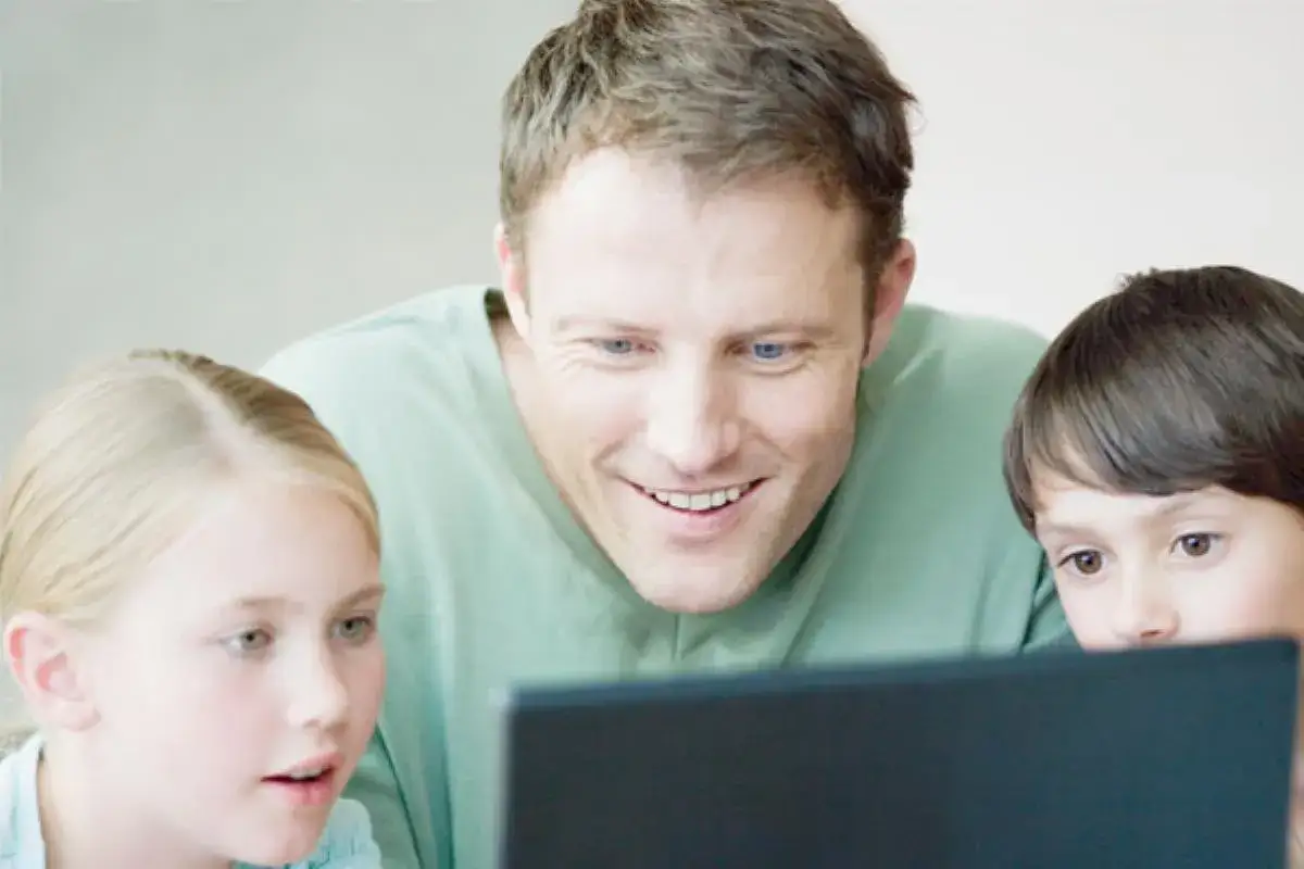Un père supervise le **contrôle parental PC** de ses enfants, partageant un moment d'apprentissage et de sécurité en ligne.