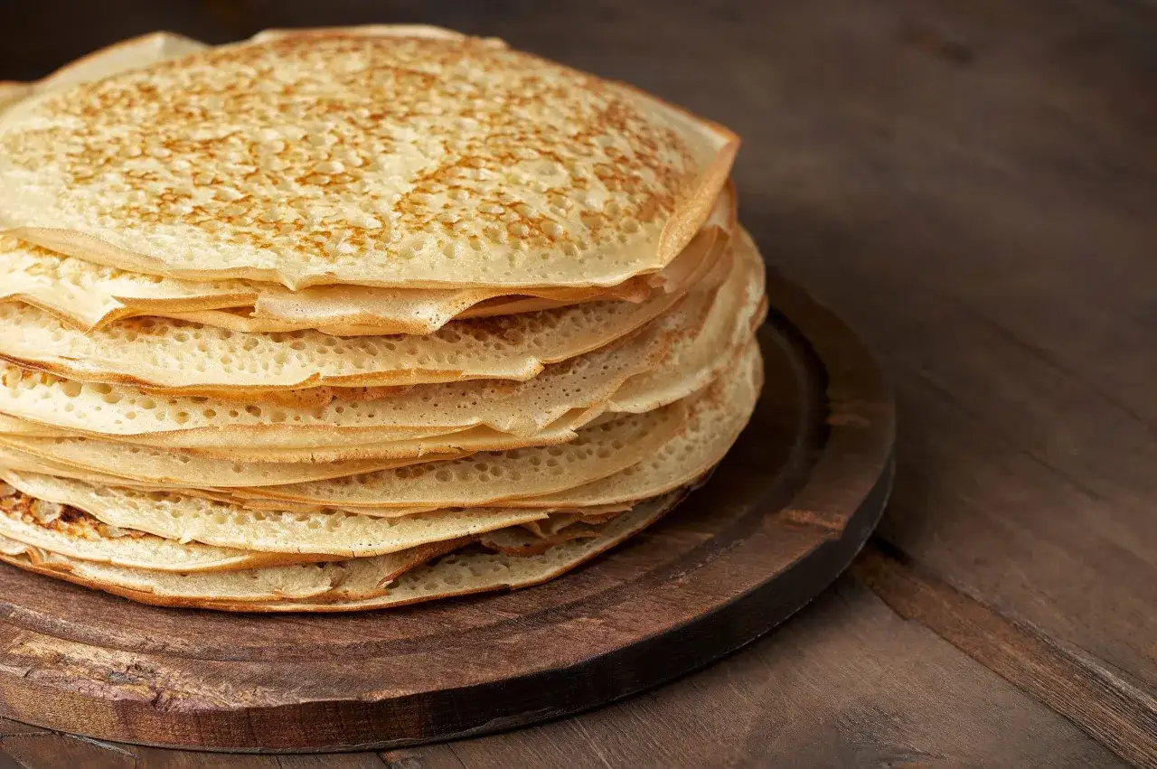 En hög med gyllene pannkakor, perfekta för ett klassiskt pannkakssmet recept. Serveras på en mörk träbricka.