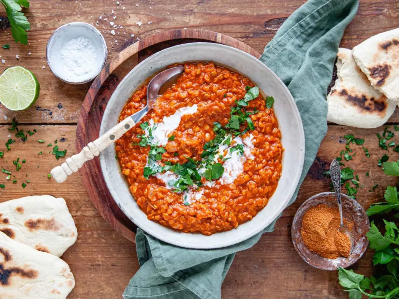 En skål med röd linsdaal, toppad med grädde och koriander, serveras med naanbröd. Ett perfekt daal recept för en mysig middag.