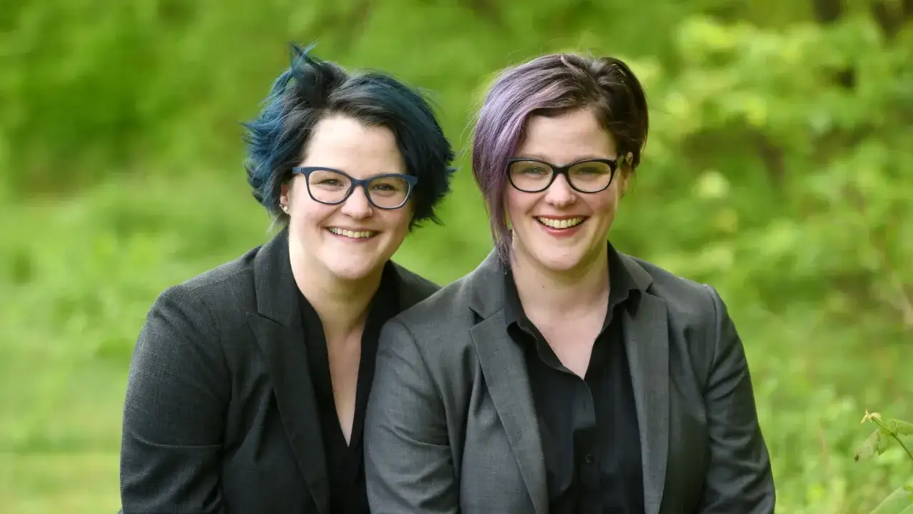 Emily Nagoski und ihre Schwester l&auml;cheln in die Kamera, beide tragen Brillen und Sakkos.