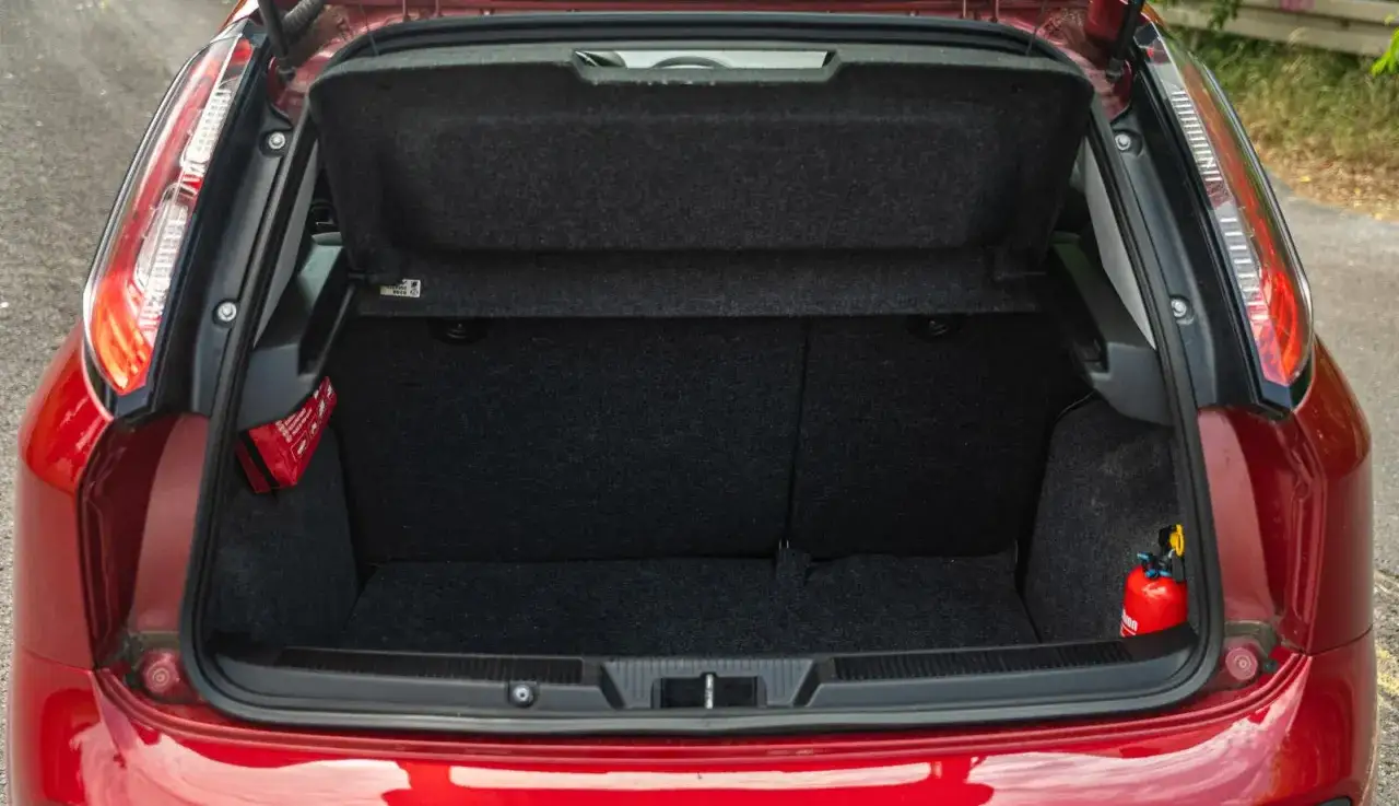 Czerwony Fiat Grande Punto z otwartym bagażnikiem. Widać apteczkę i gaśnicę.