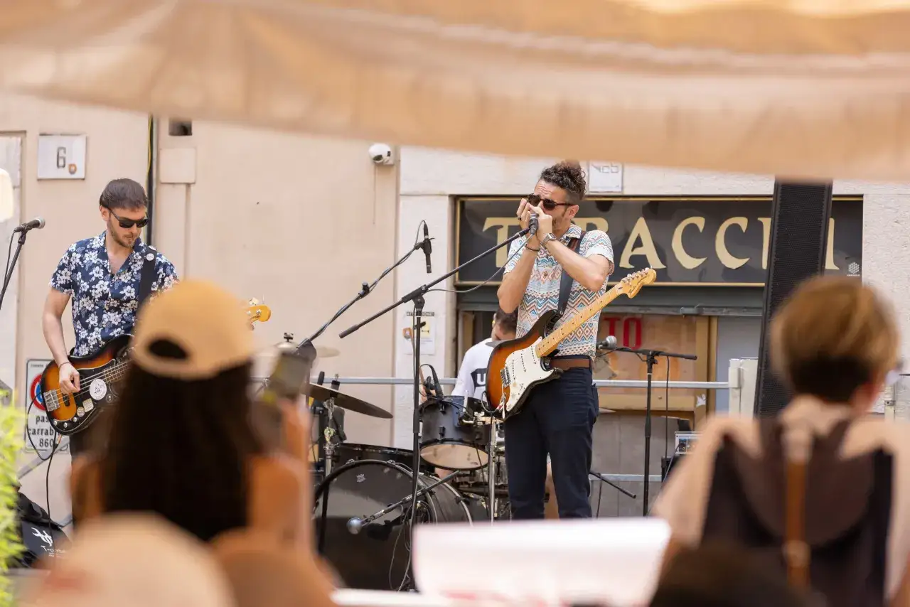 Un gruppo musicale suona per la festa della musica a Brescia. Un cantante con la chitarra e l'armonica, un bassista e un batterista.