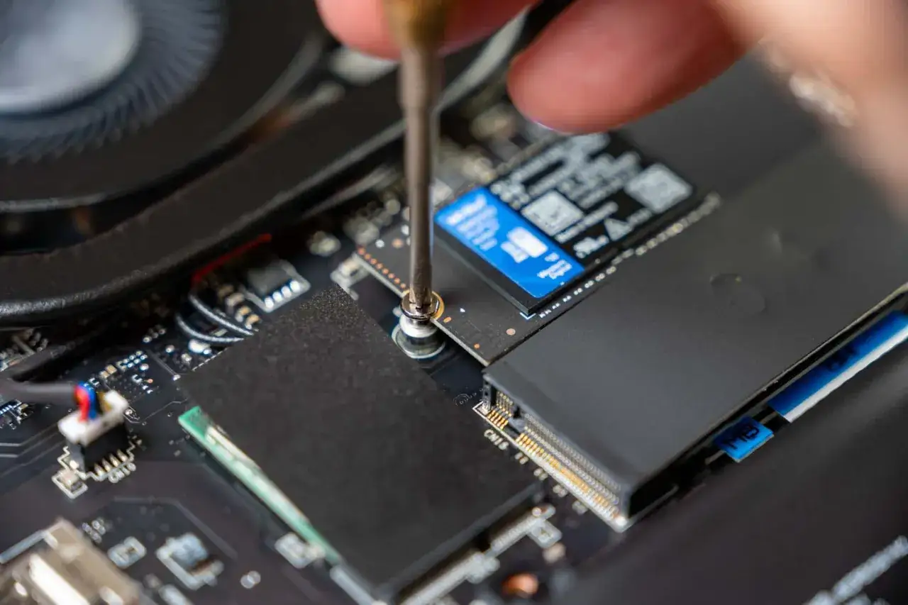 Schraubenzieher l&ouml;st Schraube, um SSD auszubauen. Nahaufnahme der Computerplatine mit L&uuml;fter und Speicherriegeln.