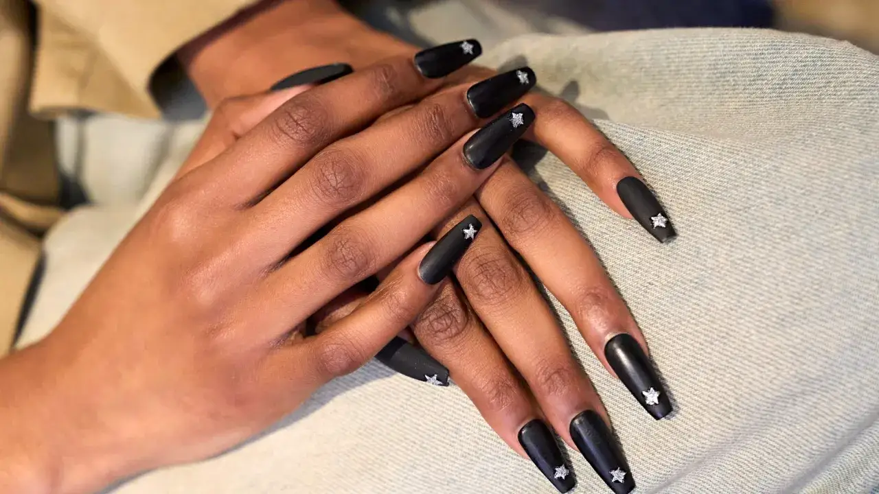 Mains aux **ongles mat** noirs, ornés d'étoiles scintillantes. Un look audacieux et chic.