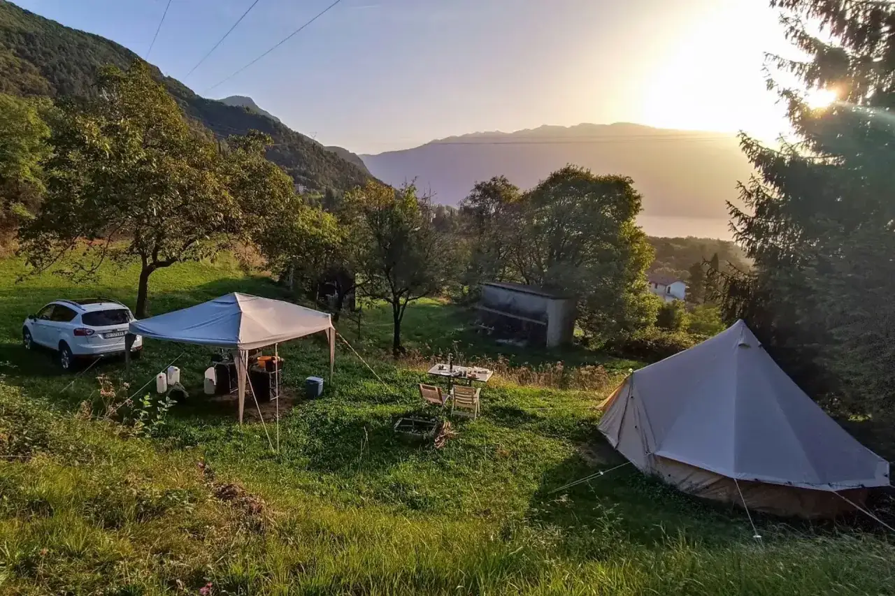 Idyllischer Campingurlaub in Deutschland: Zelte, ein Pavillon und ein Auto stehen auf einer grünen Wiese mit Bergblick im Abendlicht.