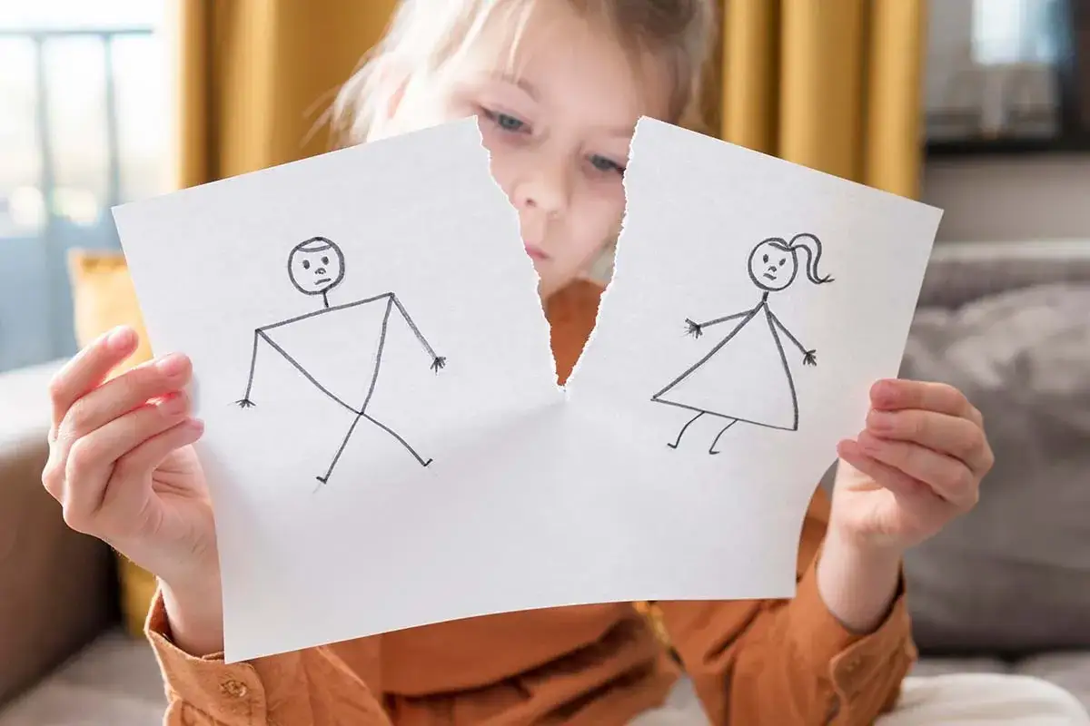 Smutna dziewczynka trzyma rozerwaną kartkę z rysunkiem rodziny. Ustalenie miejsca pobytu dziecka przy matce to dla niej nadzieja na stabilność.