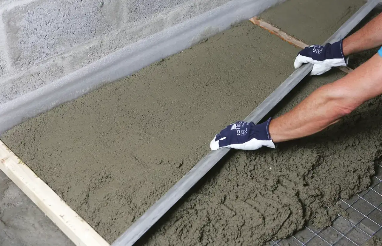 Równanie świeżego, gotowego betonu na posadzkę za pomocą łaty.