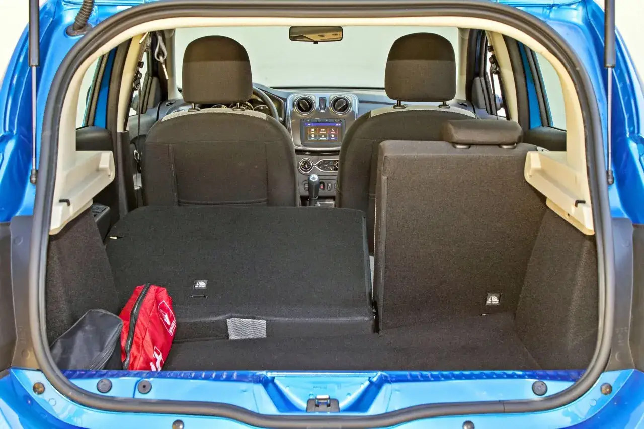 Bagażnik Dacia Sandero Stepway, gotowy na podróż. Wnętrze z podniesionymi siedzeniami, apteczka i torba. Opinie o tym aucie często podkreślają jego praktyczność.