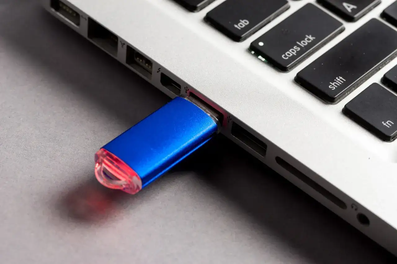 Niebieski, bootowalny pendrive podłączony do laptopa. Czerwona dioda sygnalizuje pracę urządzenia.