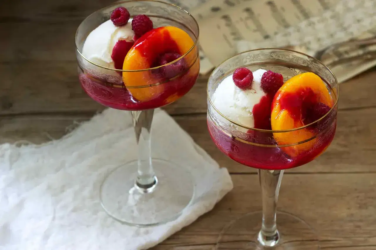 Zwei Gläser mit Pfirsich Melba: Vanilleeis, Pfirsichspalten und Himbeersauce, garniert mit frischen Himbeeren.