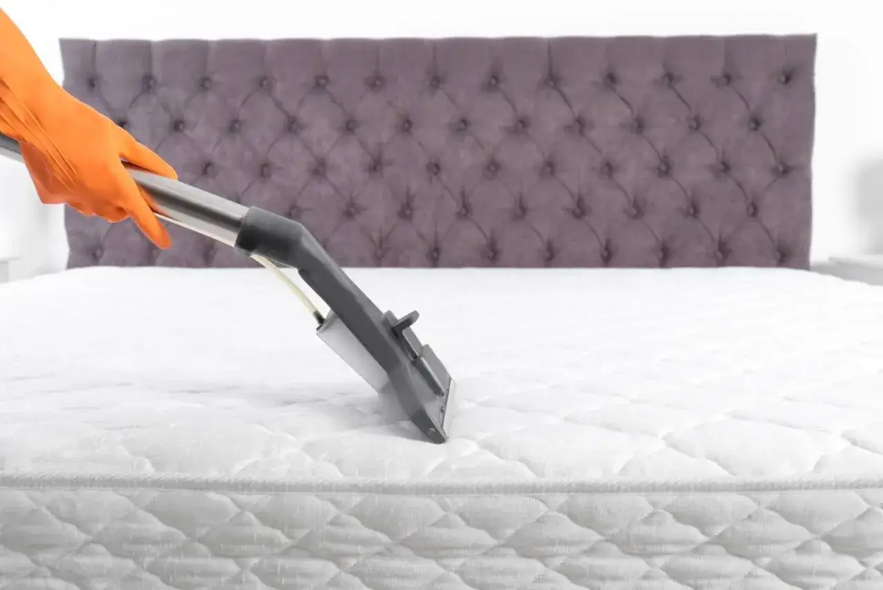 Main tenant utilise un appareil pour nettoyer matelas vapeur. Une main gant&eacute;e orange tient le manche de l'aspirateur.