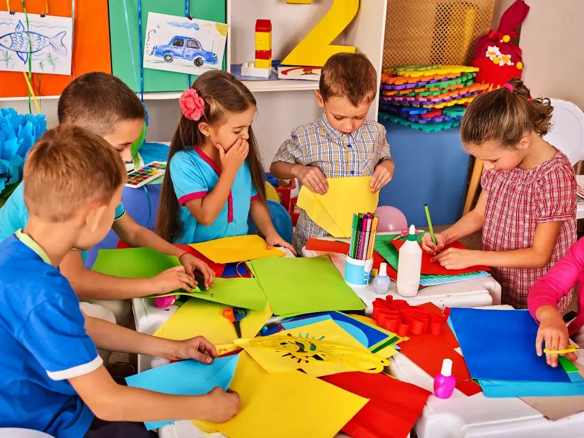 Dzieci tworzą prace plastyczne, co pokazuje innowacyjne metody nauczania w edukacji wczesnoszkolnej. Kolorowy papier, kredki i klej.
