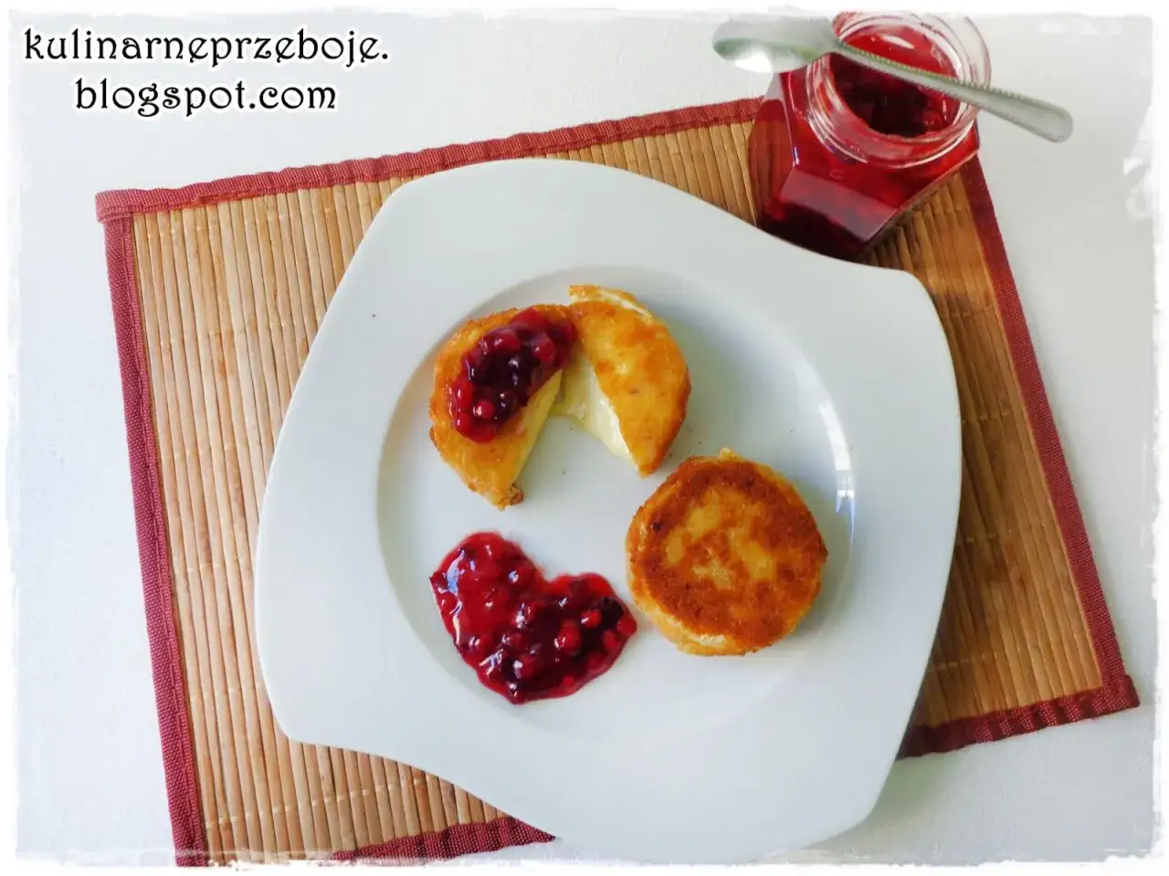 Pyszny camembert w panierce, polany konfiturą z owoc&oacute;w leśnych, kt&oacute;ra tworzy serce. Obok słoiczek z dżemem.
