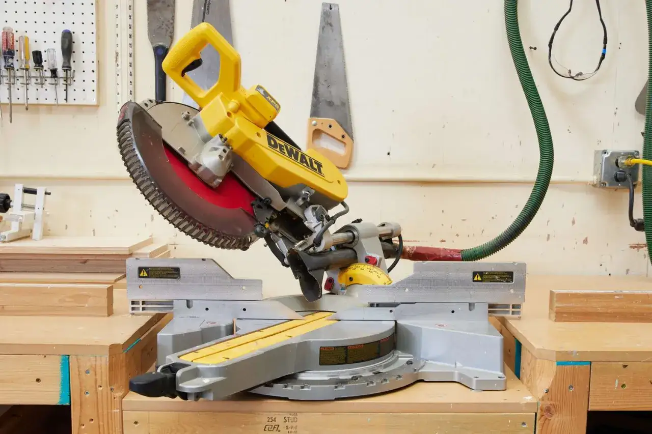 En gul DeWalt kap- och geringssåg står på ett arbetsbord. Ovanför hänger olika sågar på väggen, redo för projekt.