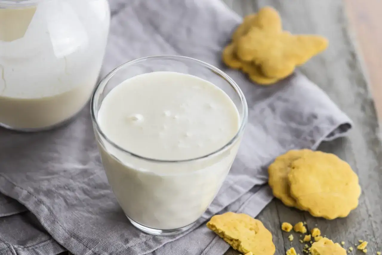 Verre de lait ribot &eacute;quivalent, avec des biscuits sabl&eacute;s en forme de papillon et de fleur sur une serviette grise.