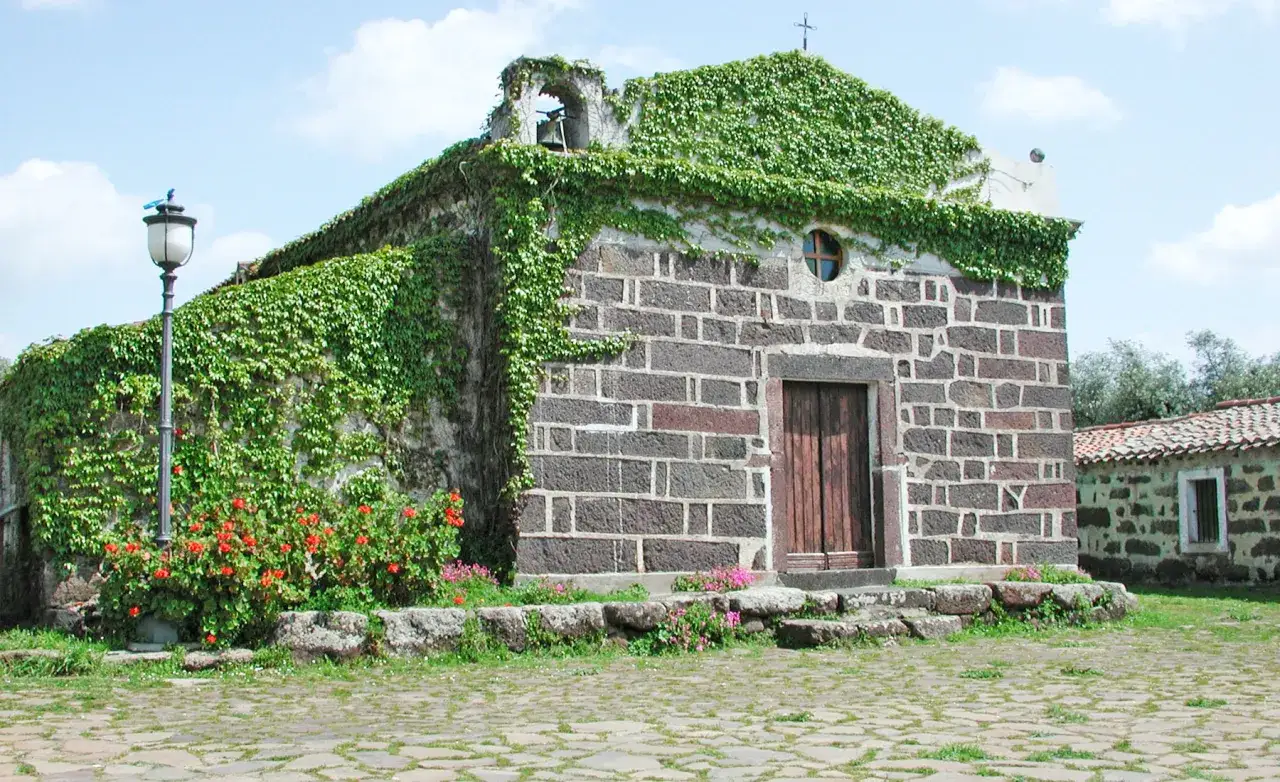 Chiesa ricoperta di edera a Paulilatino, cosa vedere: un'antica costruzione in pietra con fiori rossi e un lampione.