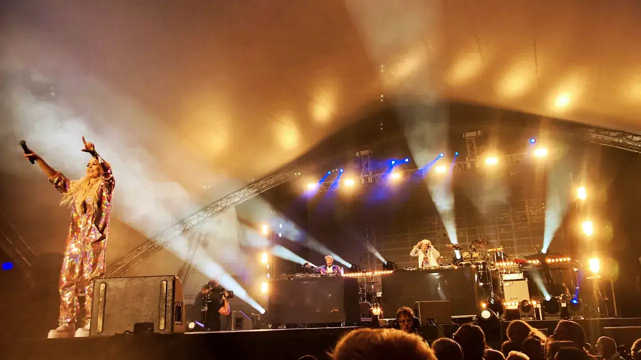 En kvinna i glittrig dräkt sjunger på scen, omgiven av rök och ljus. En del av en **svenska artister lista** på en stor konsert.