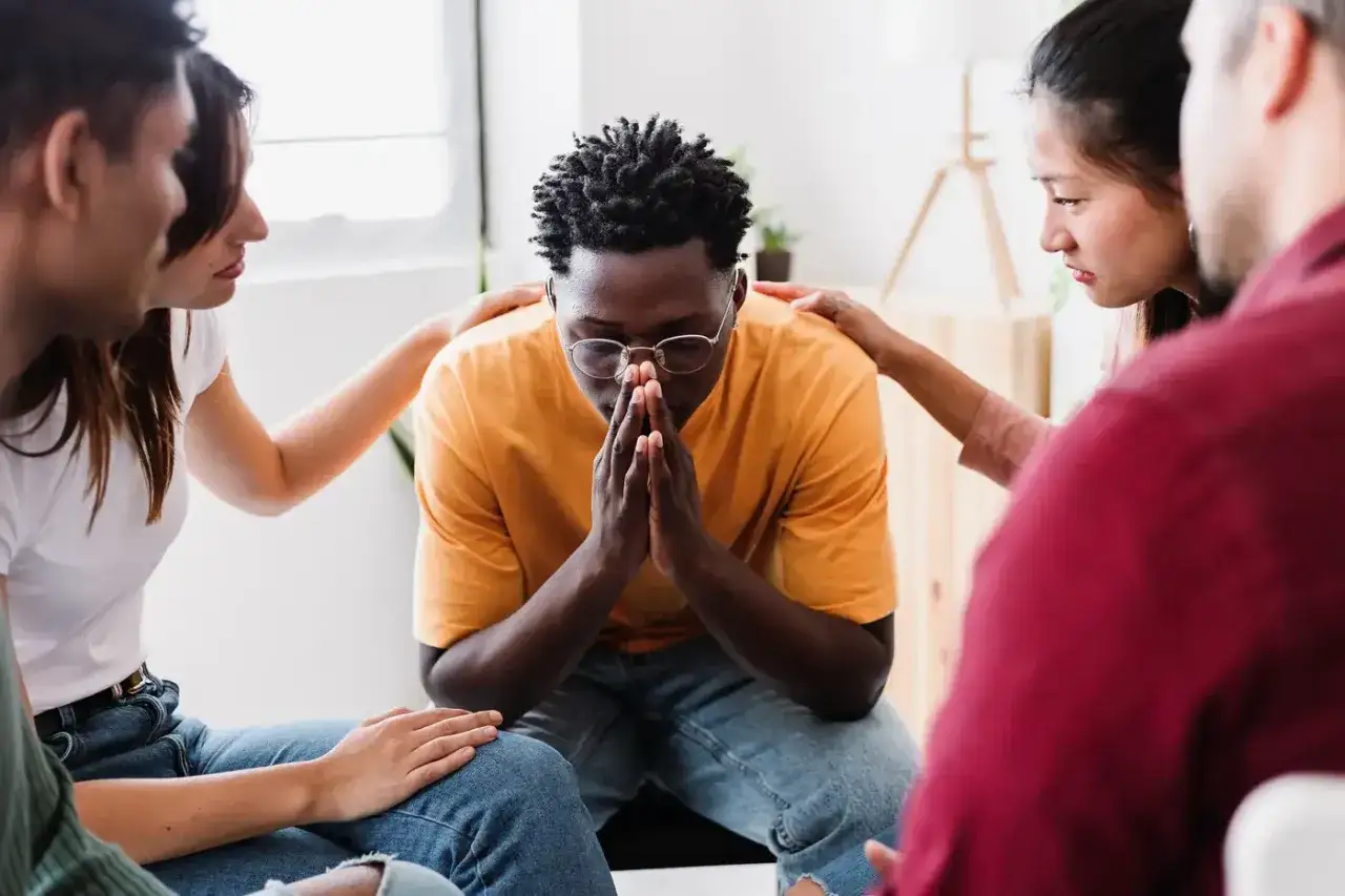 Un grupo de personas muestra apoyo a un hombre con las manos juntas, demostrando responsabilidad emocional y empat&iacute;a en un momento de vulnerabilidad.