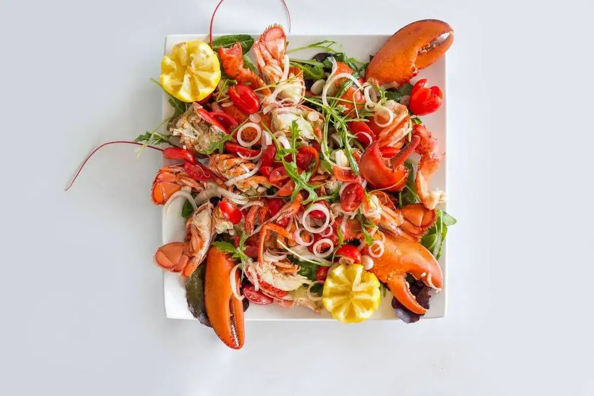Insalata di mare con aragosta, pomodorini, cipolla e limone, un piatto fresco e colorato, perfetto per un'estate da gustare.