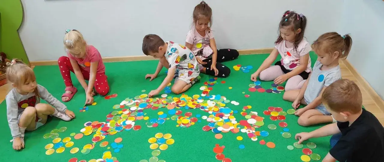 Dzieci bawią się kolorowymi kółkami na zielonej macie. To może być część zajęć, za które płacimy jako opłata za przedszkole 6-latki.