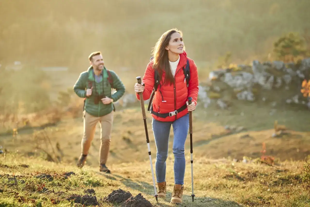 Para, co to jest trekking? Para wędruje po wzgórzach w jesiennym słońcu, ciesząc się aktywnością na świeżym powietrzu.