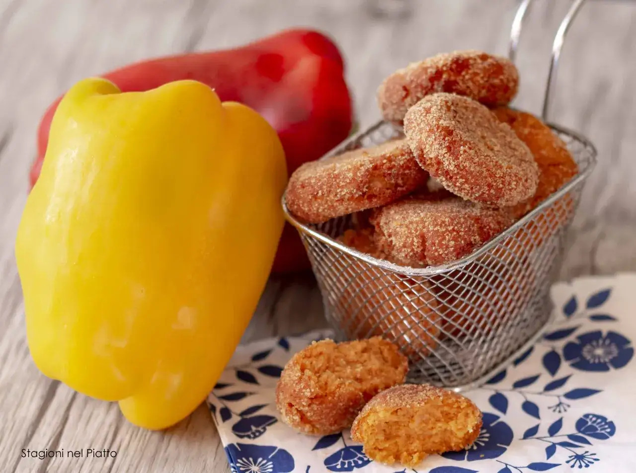 Polpette di peperoni dorate e croccanti, accanto a peperoni freschi gialli e rossi.