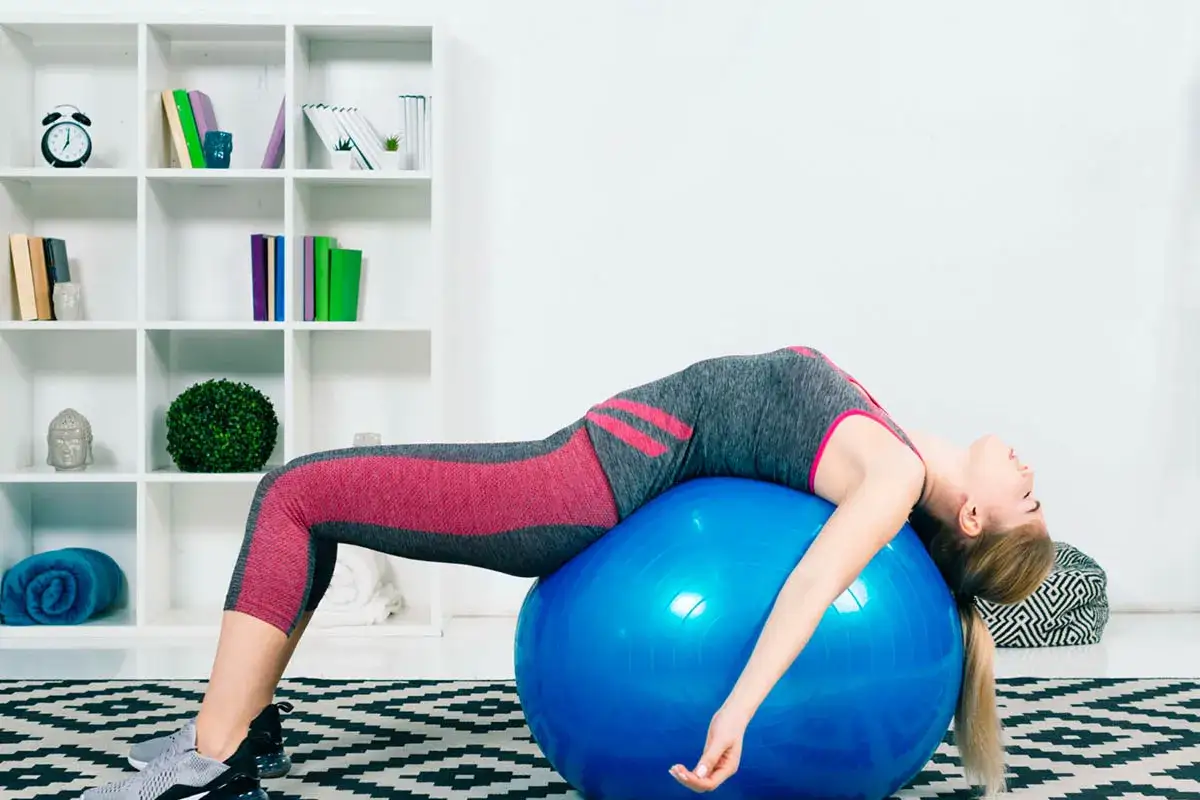 Femme effectuant un exercice lombaire sur un gros ballon bleu, le dos cambr&eacute;.