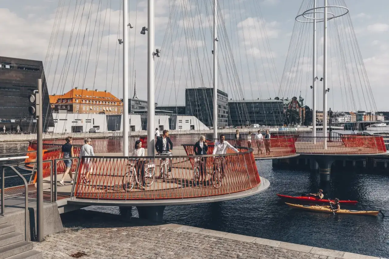 Ponte ciclabile a Copenaghen, dove le biciclette gratis sono un modo di vivere. Persone passeggiano e pedalano su un ponte moderno con ringhiere rosse.