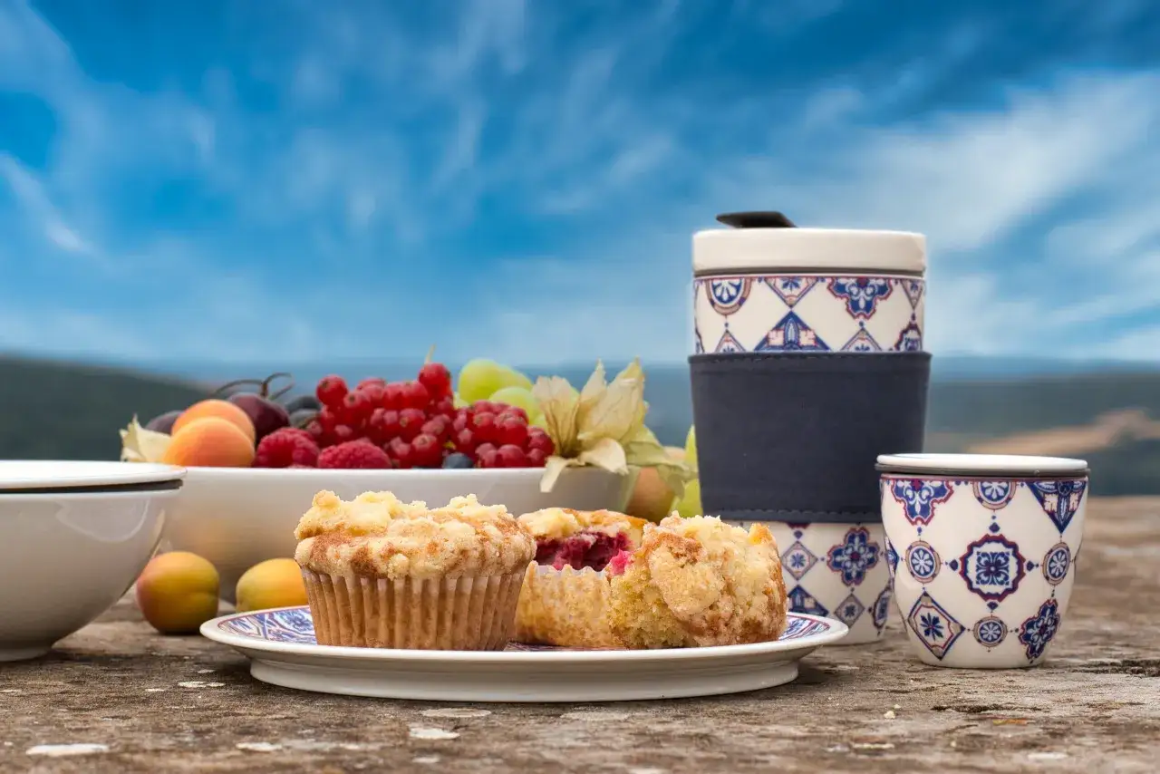 Himbeer Muffins mit Streuseln auf einem Teller, daneben Obstschale und Becher mit blauem Muster.