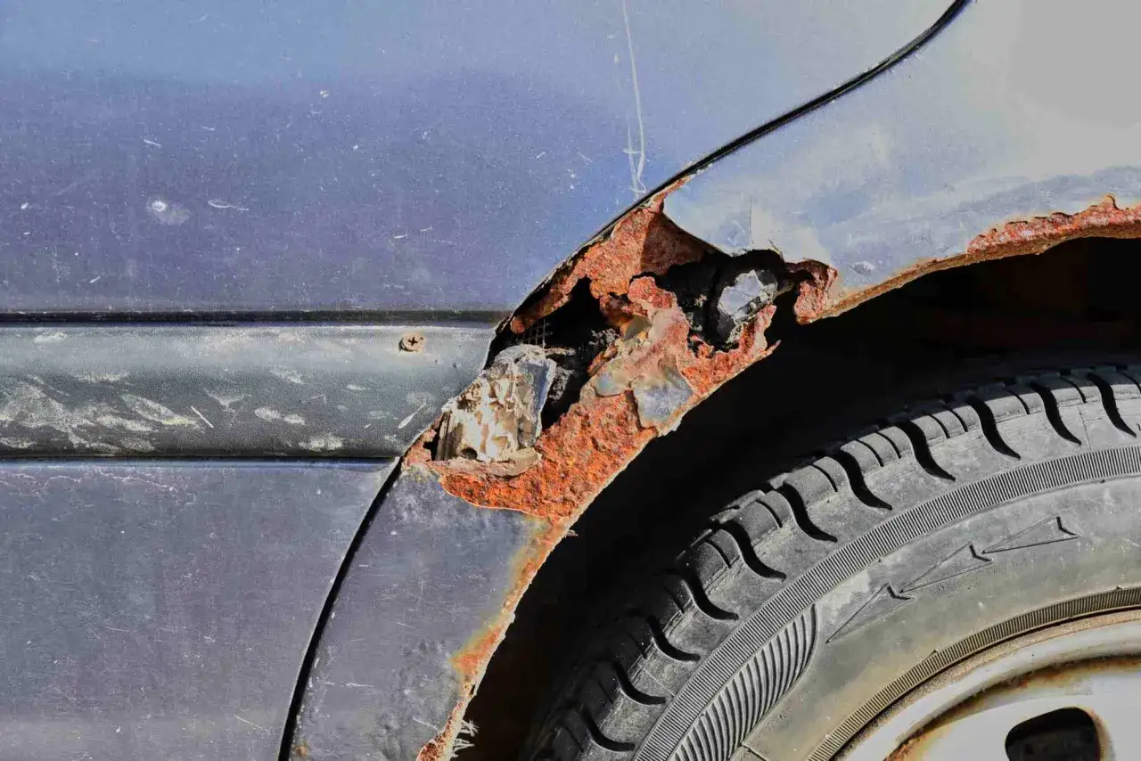Starker Rost unter dem Lack am Kotfl&uuml;gel eines Autos. Die Rostschicht ist dick und br&ouml;ckelt ab, was zeigt, wie wichtig es ist, Rost unter Lack zu entfernen, bevor er das Metall zerst&ouml;rt.