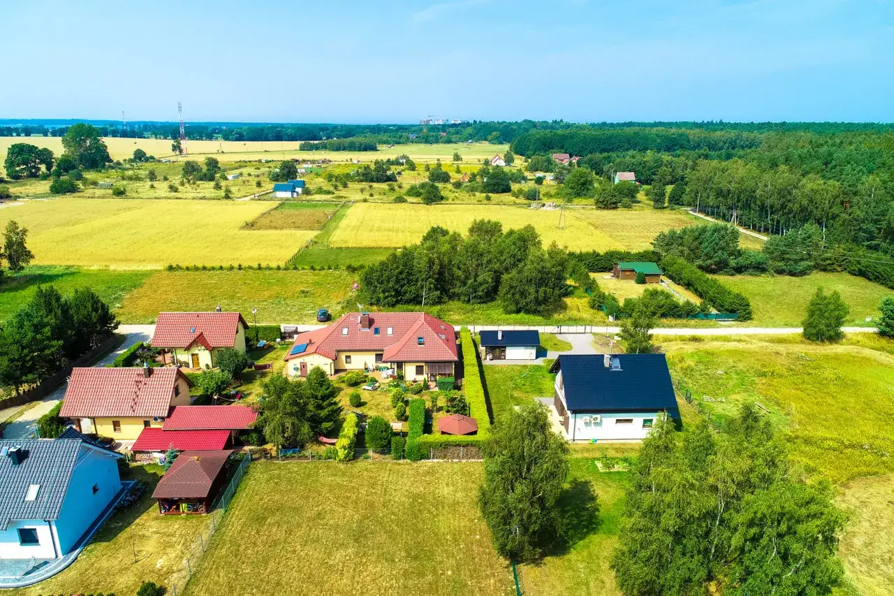 Domy z czerwonymi dachami na tle pól i lasów. Warto sprawdzić, jaki podatek za działkę budowlaną obowiązuje w tej okolicy.