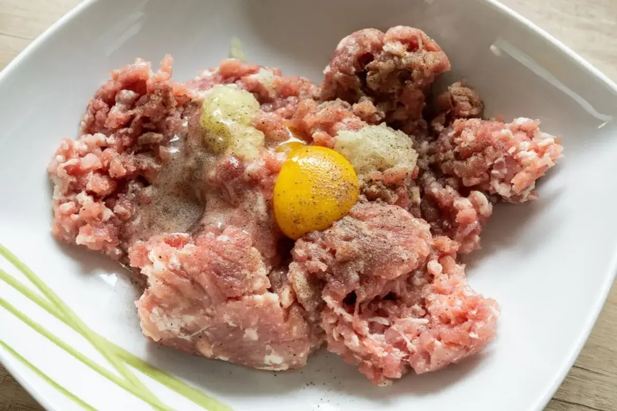 Mielone mięso wieprzowe z jajkiem i przyprawami, gotowe do formowania kotletów mielonych.